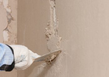 Hand with a spatula in the process of leveling the raw plaster.